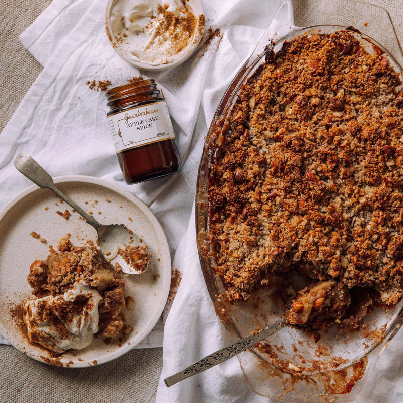 Apple crumble pie with a scoop taken out, next to a jar of spice and a plate with a serving.