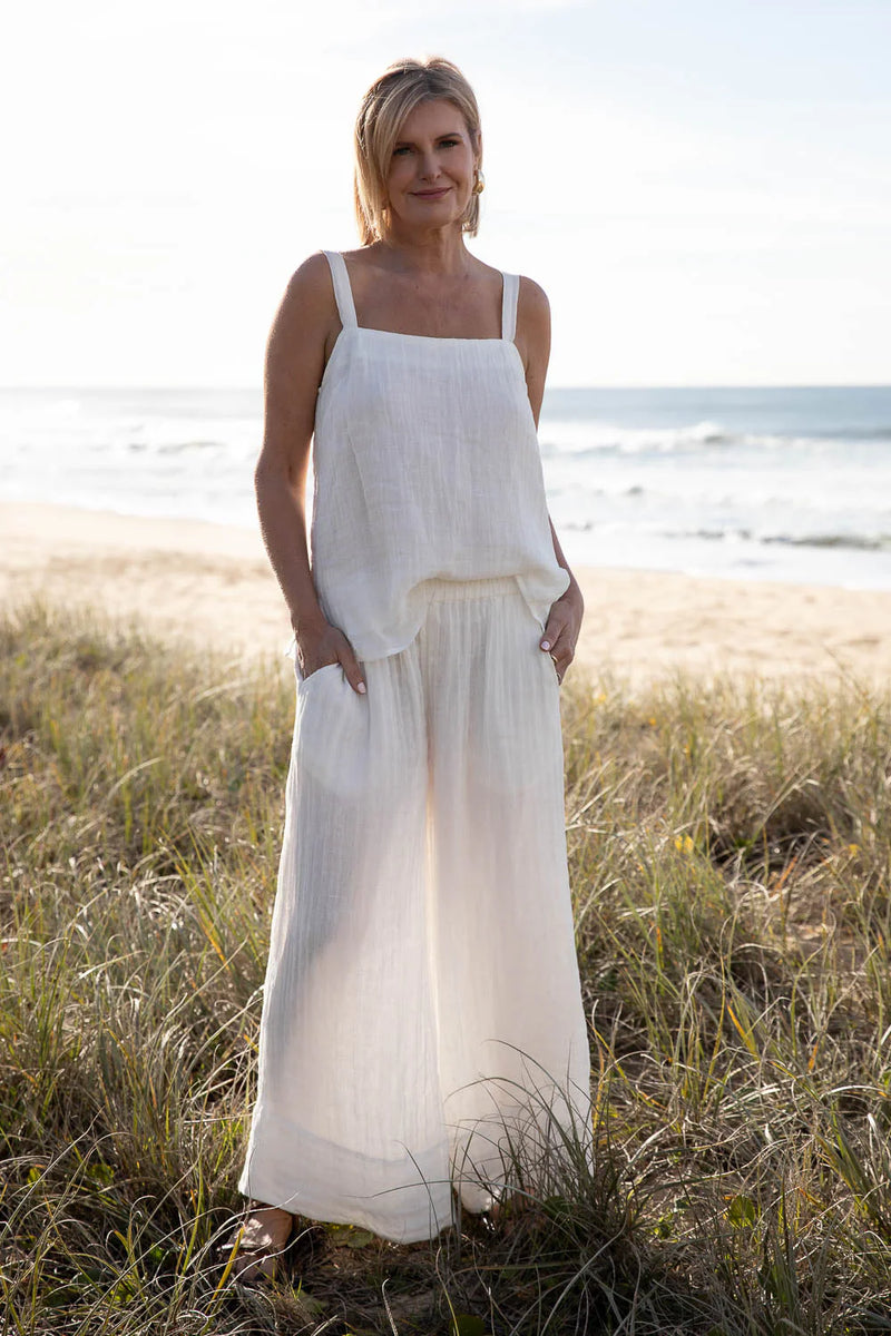 Woman in a white dress standing on a grassy beach with ocean in the background