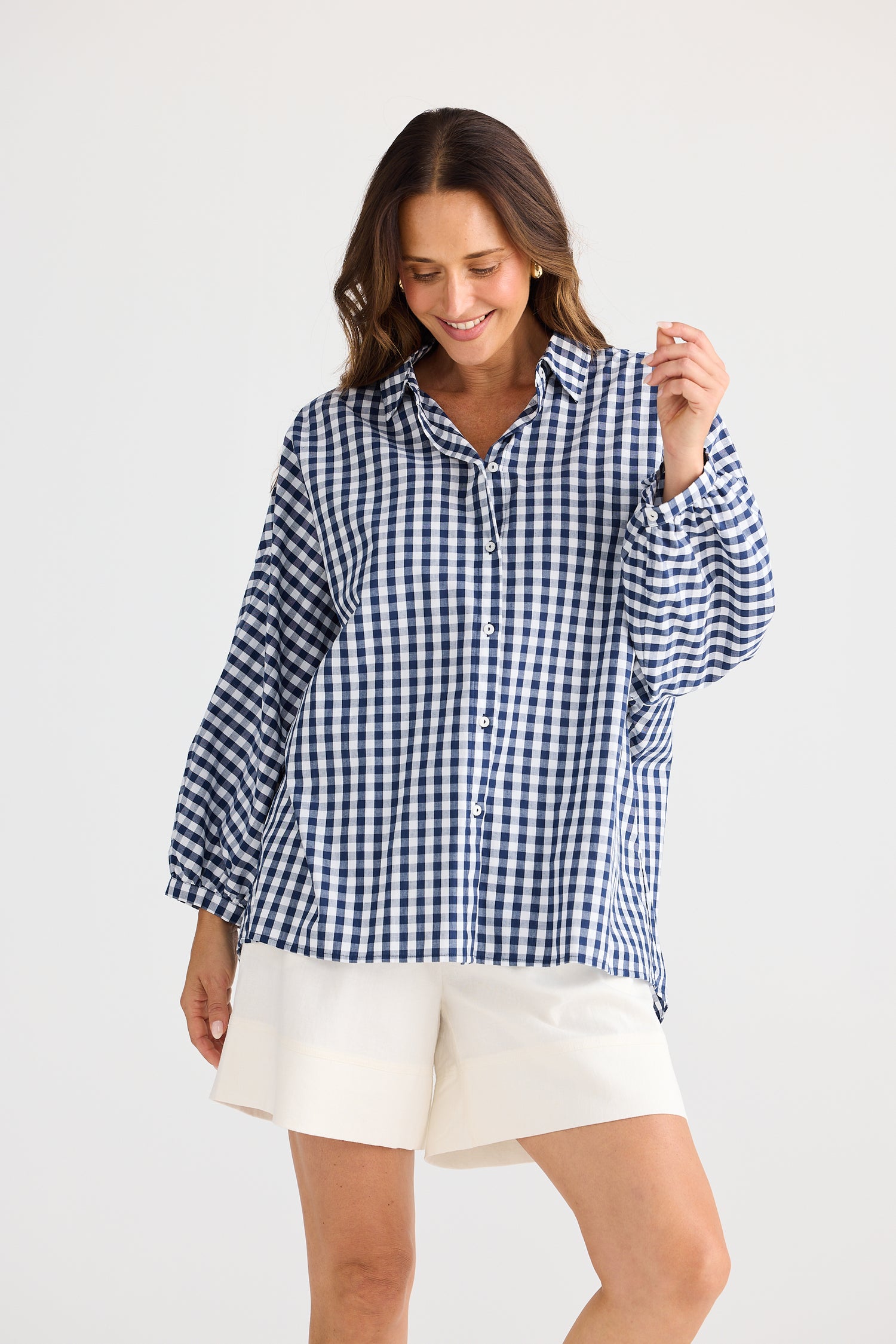 Woman wearing a blue and white checkered shirt and white shorts on a light gray background