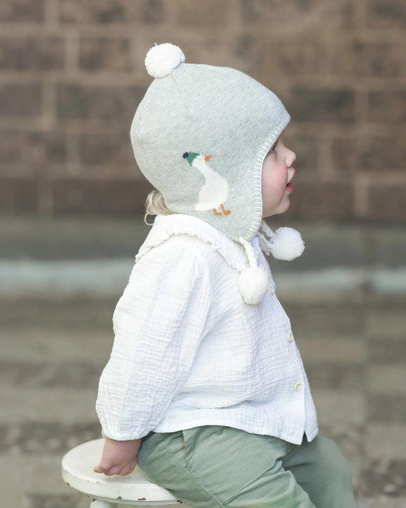 Child wearing a light gray knit hat with a white bird design and pom-pom, sitting on a step. Toshi Baby Blouse Peter Pan Cream