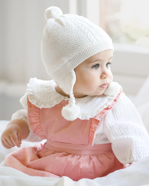 Baby wearing a white knit hat and pink dress with a white lace collar.