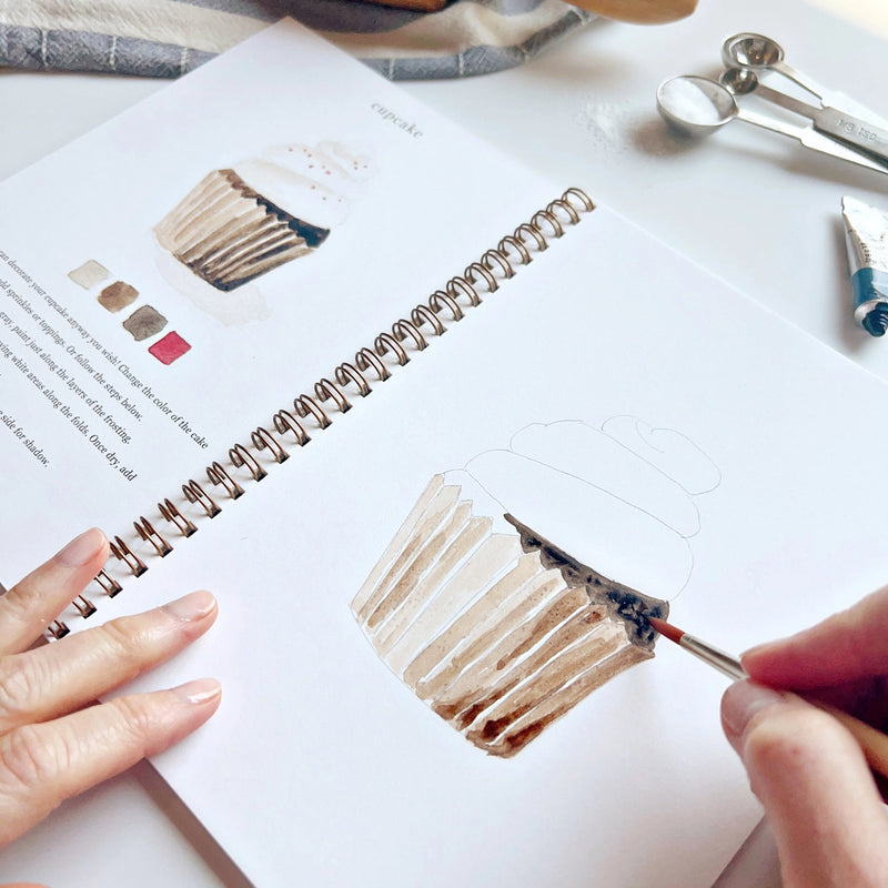 Person painting a color swatch on a book with a paintbrush