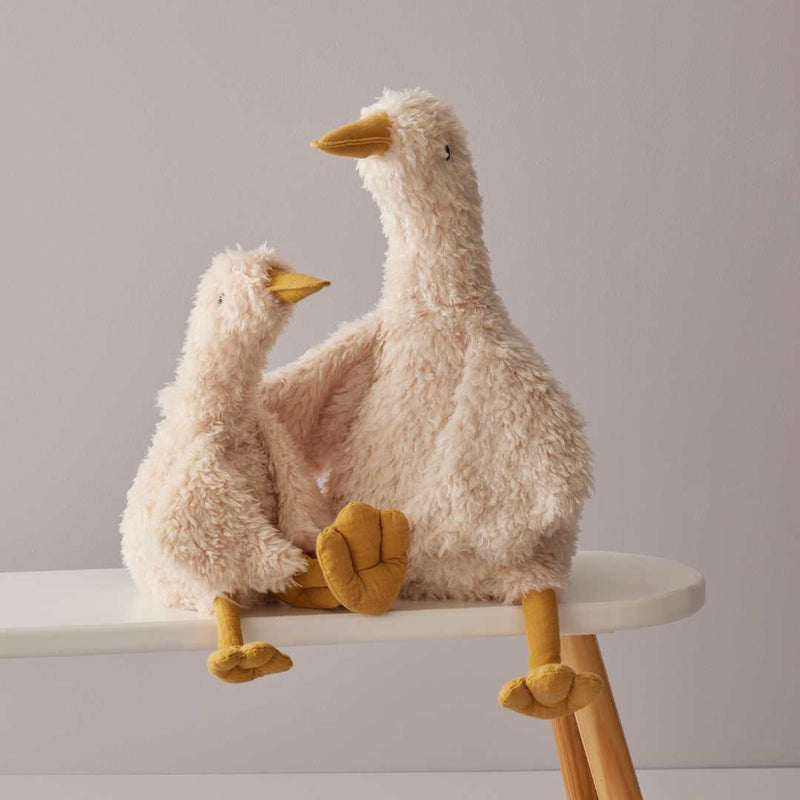 Two fluffy goose plush toys on a small stool against a plain background