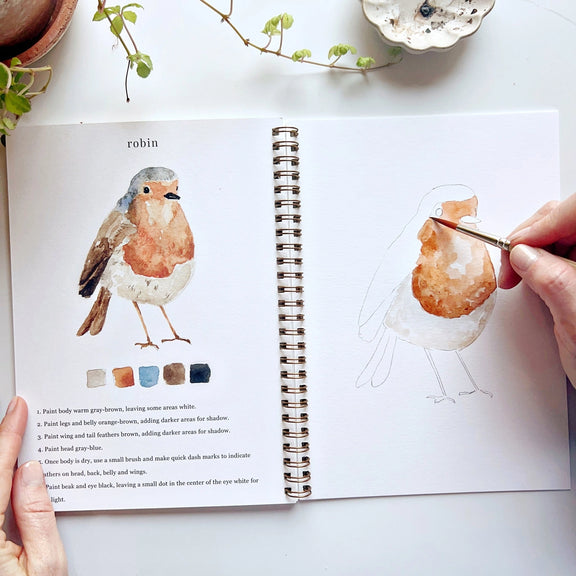 Open book with illustration of a robin and hand holding a paintbrush