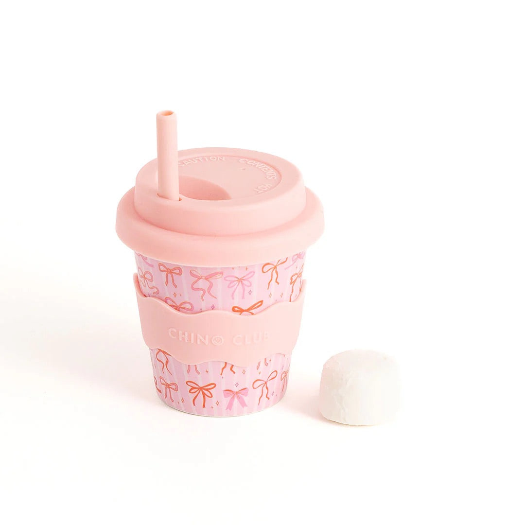 Pink tumbler with bow pattern and straw on a white background by Chino Club