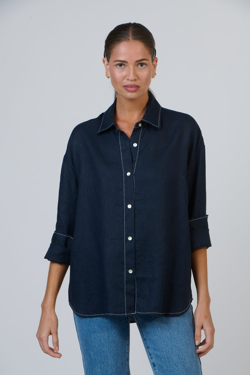 Woman wearing a dark navy blue button-up linen shirt against a plain background