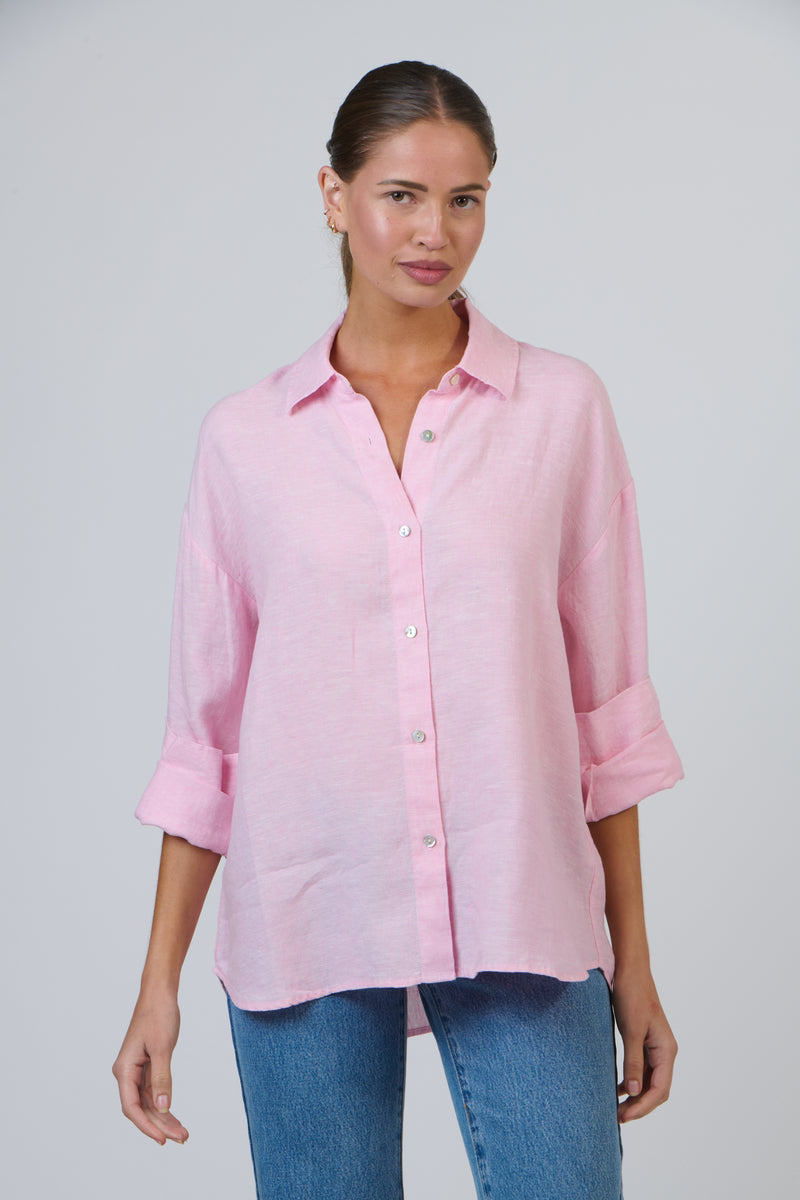 Woman wearing a pink linen shirt and blue jeans against a gray background