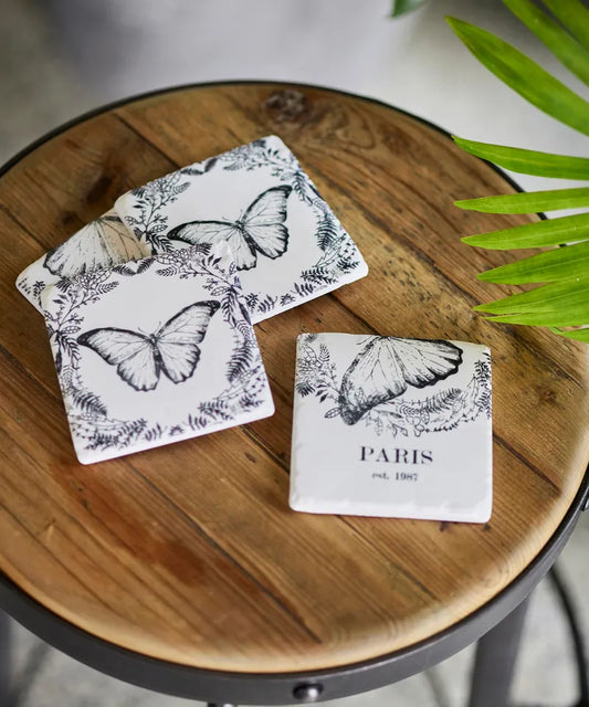 Butterfly-themed coasters on a wooden surface with a plant in the background