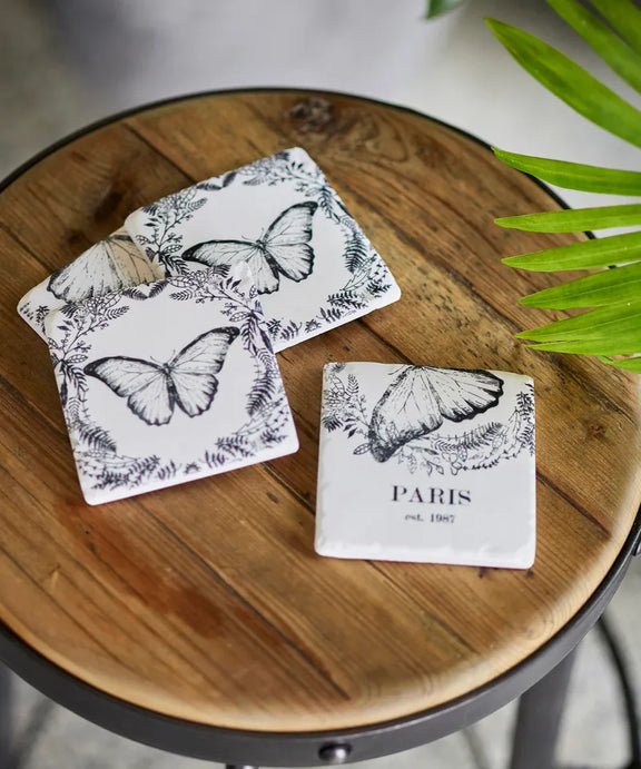 Butterfly-themed coasters on a wooden surface with a plant in the background