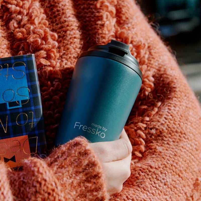 Person holding a emerald green Made By Fressko Camino tumbler with a plaid patterned box in the background