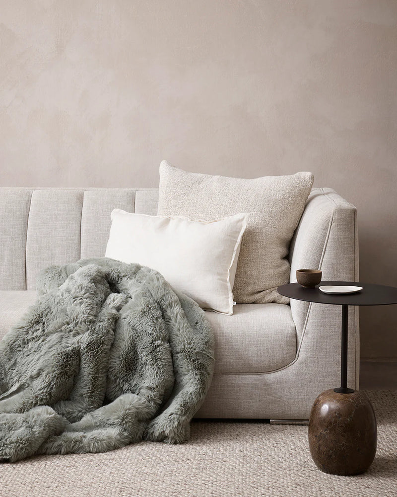 Gray sofa with a fluffy gray throw blanket and a small side table in a neutral room. BayaLiving 60x60 oatmeal artisan weave cushion
