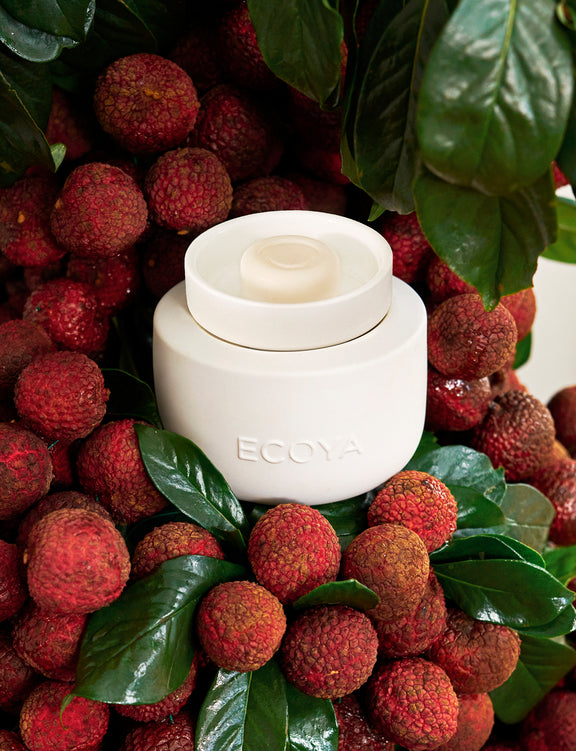 White Ecoya candle surrounded by red fruits and green leaves