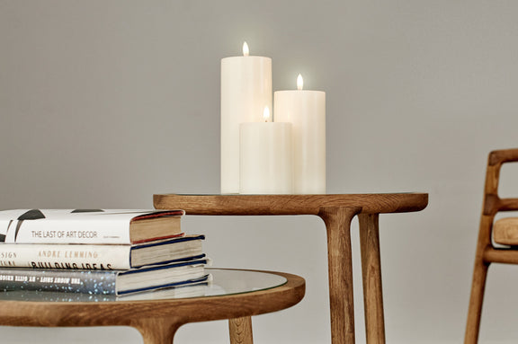 Wooden table with books and three classic ivory flameless candles on a plain background