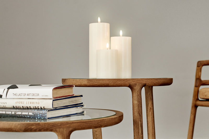 Wooden table with books and three classic ivory flameless candles on a plain background