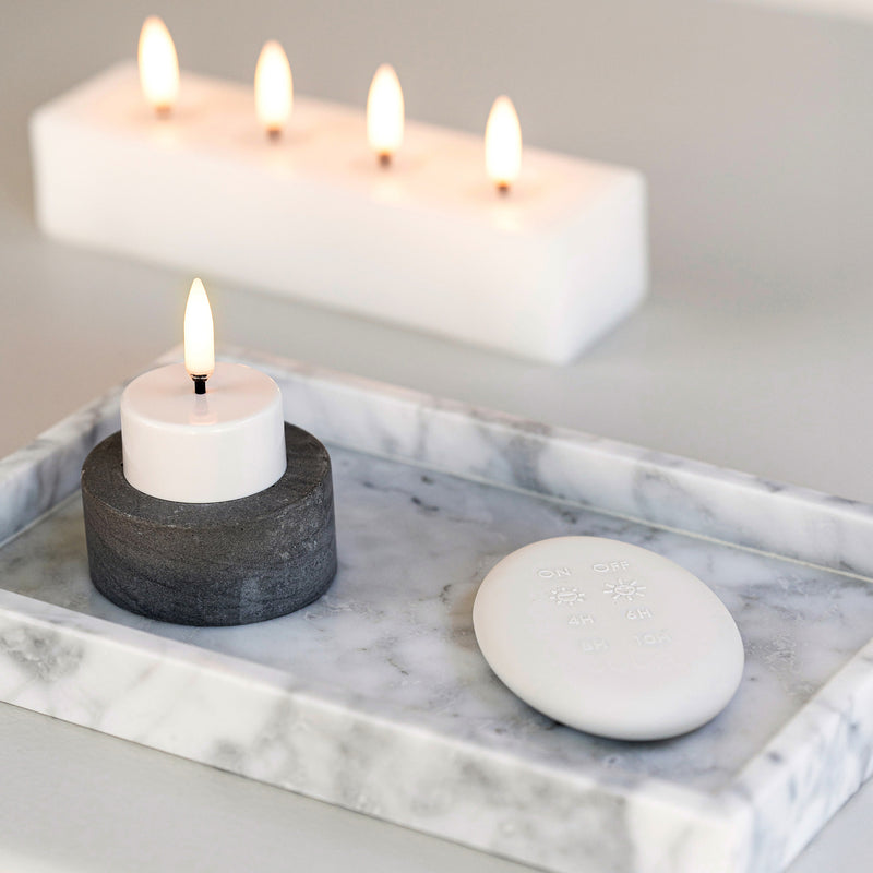 Candle in a black holder on a marble surface with a blurred white candle in the background.