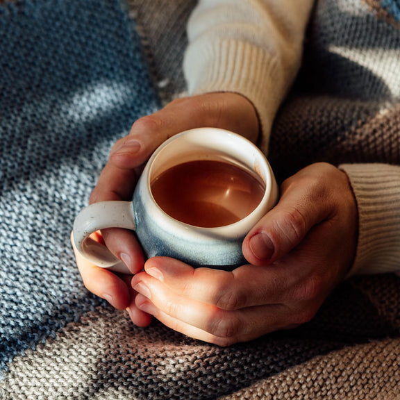 Hands holding a mug of hot chocolate against a cozy blanket background