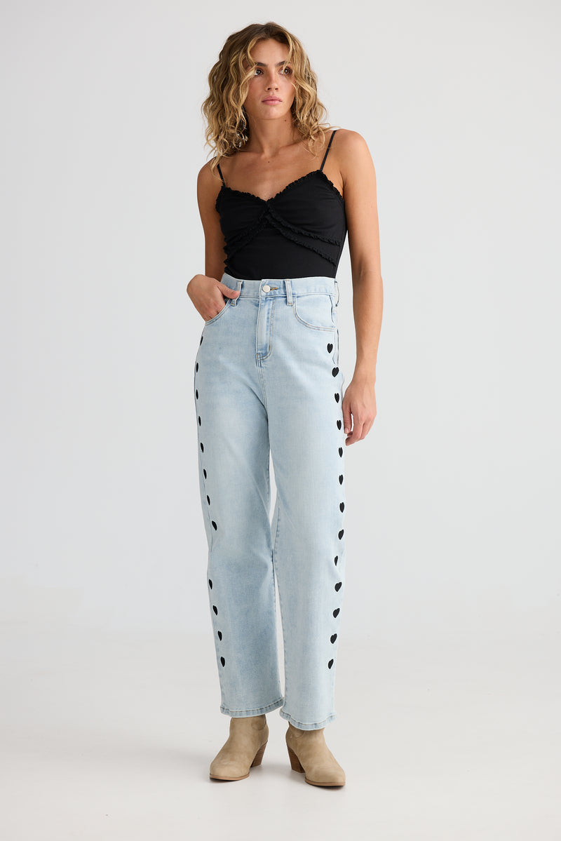 Woman wearing light blue jeans with black heart patterns on a white background