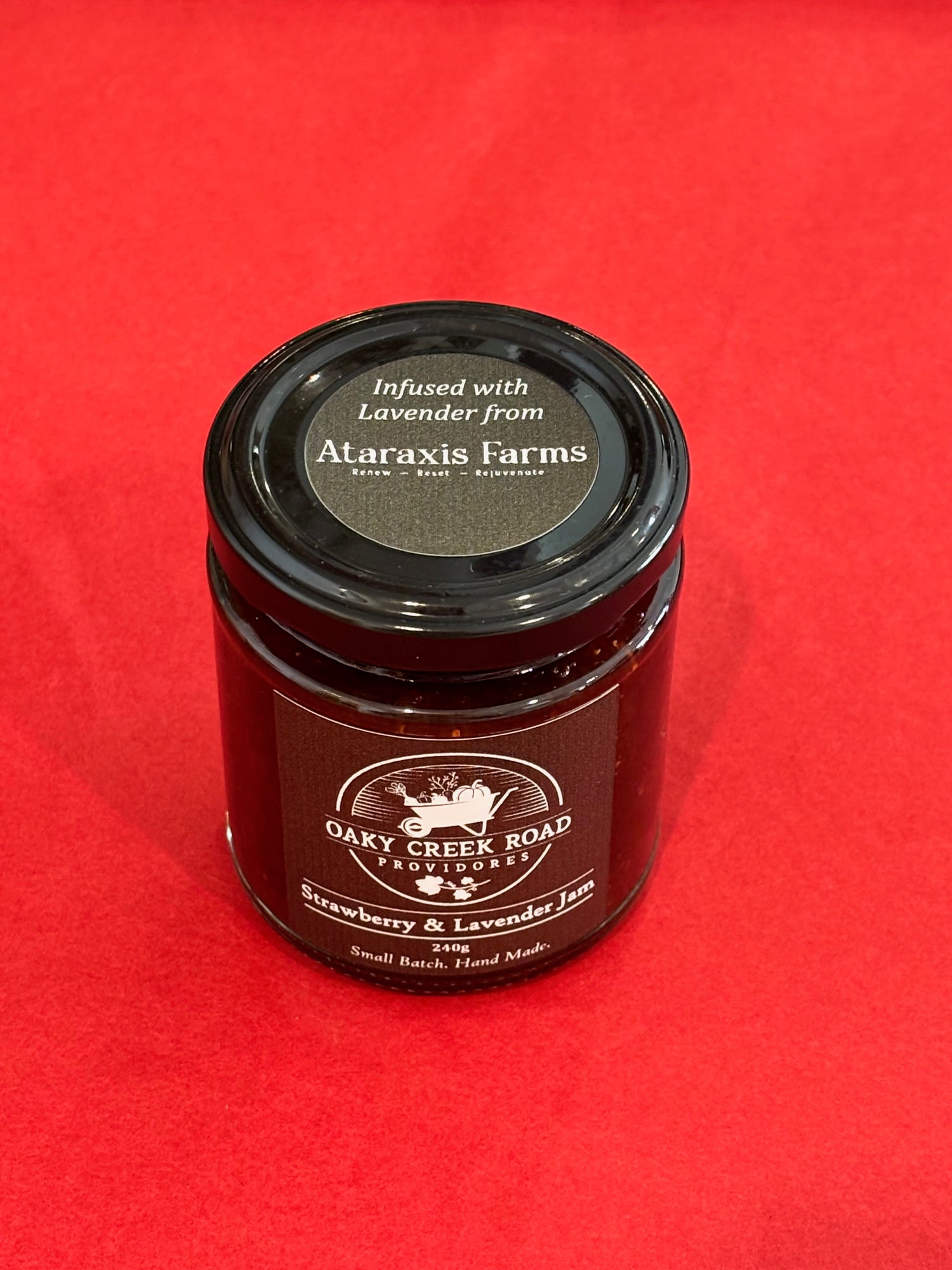Jar of strawberry and lavender jam with a black lid on a red background