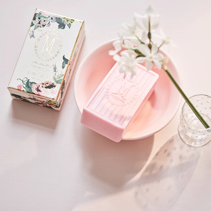 Pink soap bar on a pink plate with a decorative box and white flowers on a light background