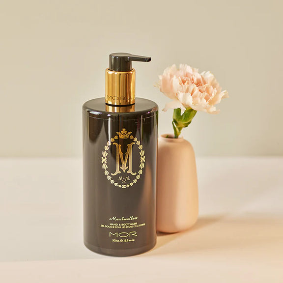 Black bottle with gold pump and decorative logo next to a pink flower in a vase on a light background - mor marshmallow wash available at my country escape australia