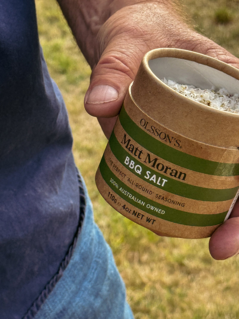Hand holding a container of Matt Moran BBQ Salt with a grassy background