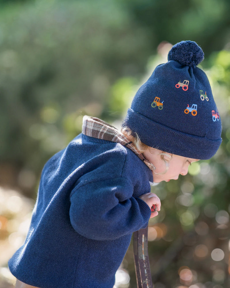 Child wearing a blue knit hat with embroidered tractor designs outdoors