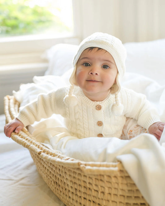 Baby in a white outfit sitting in a wicker basket with a soft white blanket.