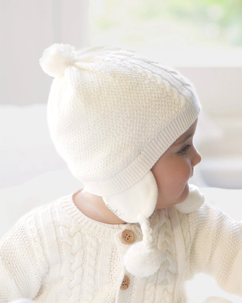 Baby wearing a white knit hat and sweater with a blurred background