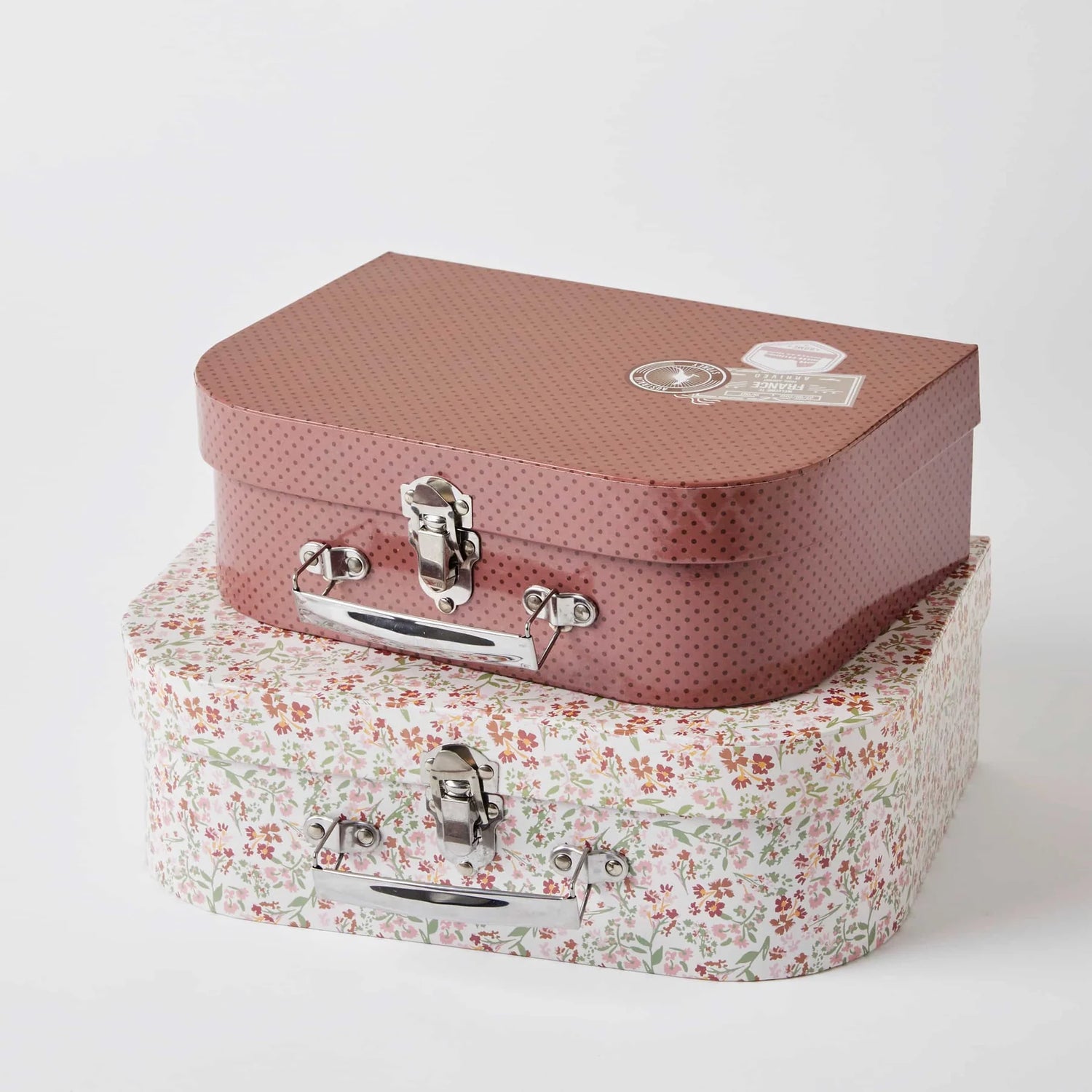 Two vintage-style suitcases, one pink with a pattern and one floral, on a white background. Play suitcases.