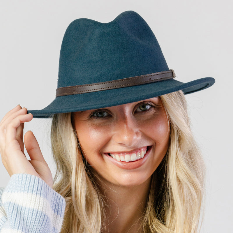 Woman wearing a blue fedora hat with a brown band on a light gray background