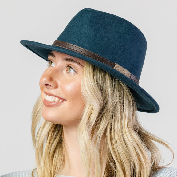 Woman wearing a blue fedora hat with a brown band on a light gray background