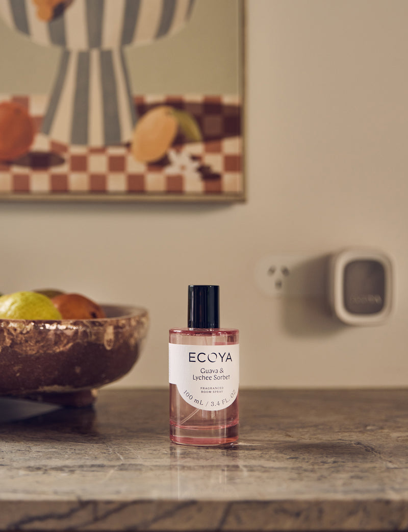 Ecoya bottle on a countertop with a decorative mirror and fruit bowl in the background