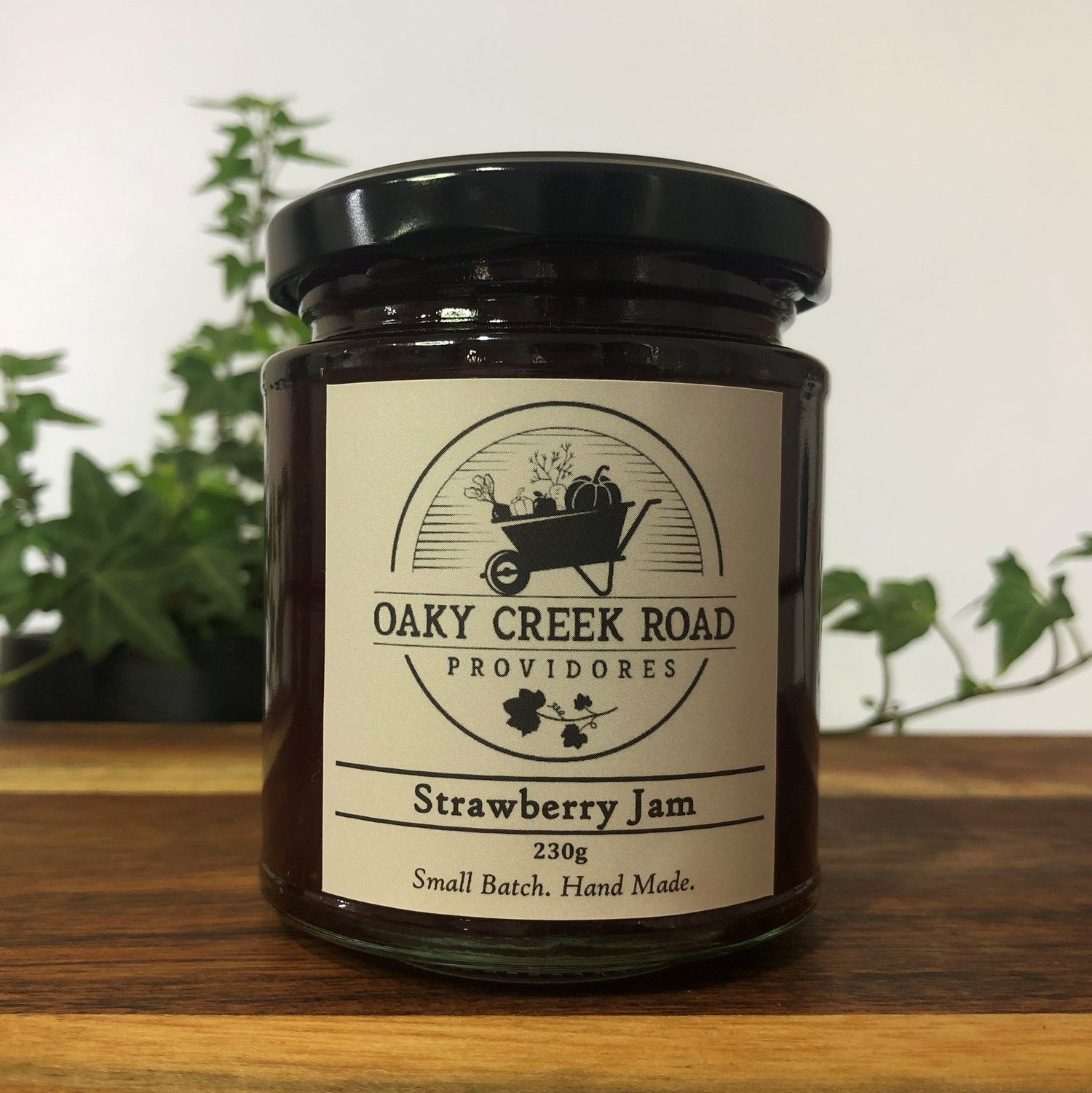 Jar of strawberry jam from Oaky Creek Road Providores on a wooden surface with plants in the background