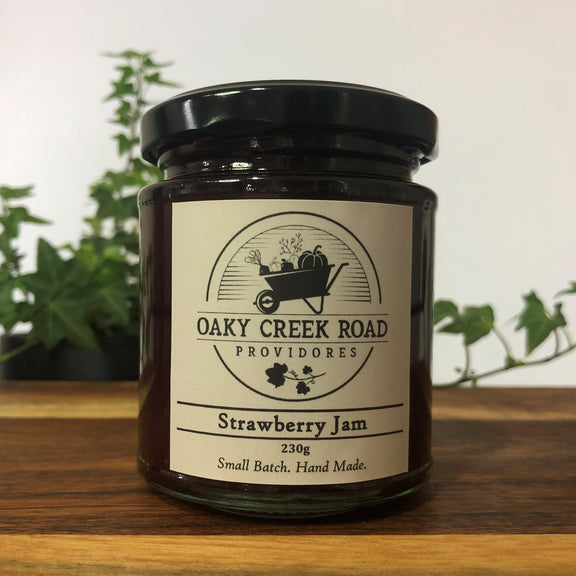 Jar of strawberry jam from Oaky Creek Road Providores on a wooden surface with plants in the background