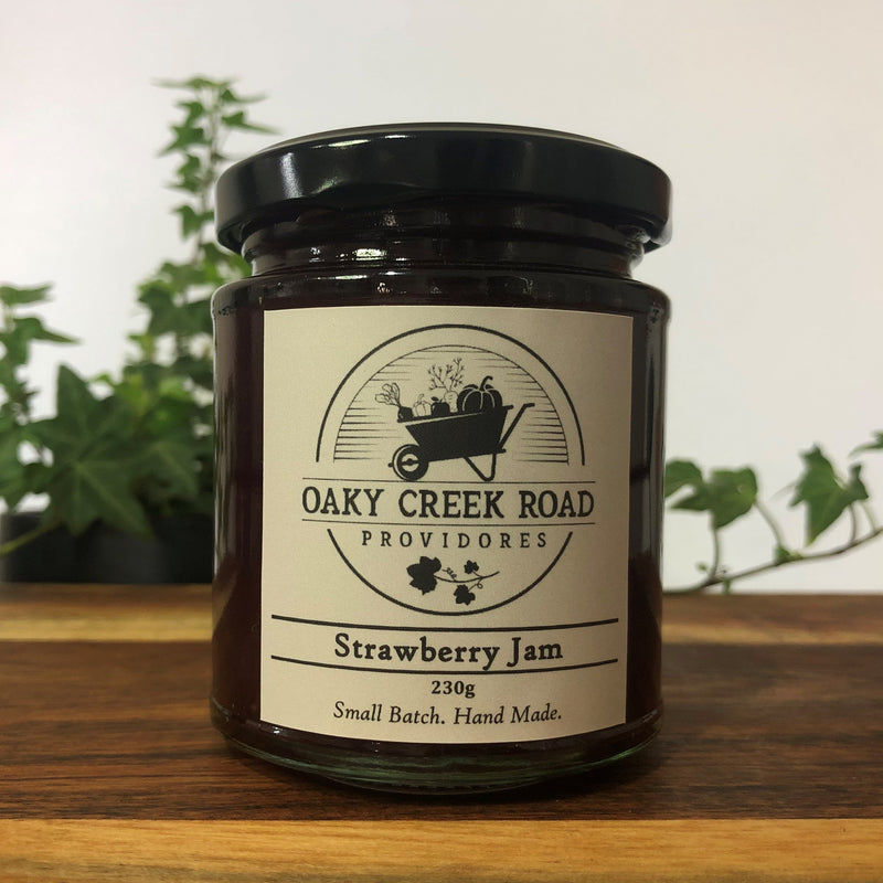 Jar of strawberry jam from Oaky Creek Road Providores on a wooden surface with plants in the background