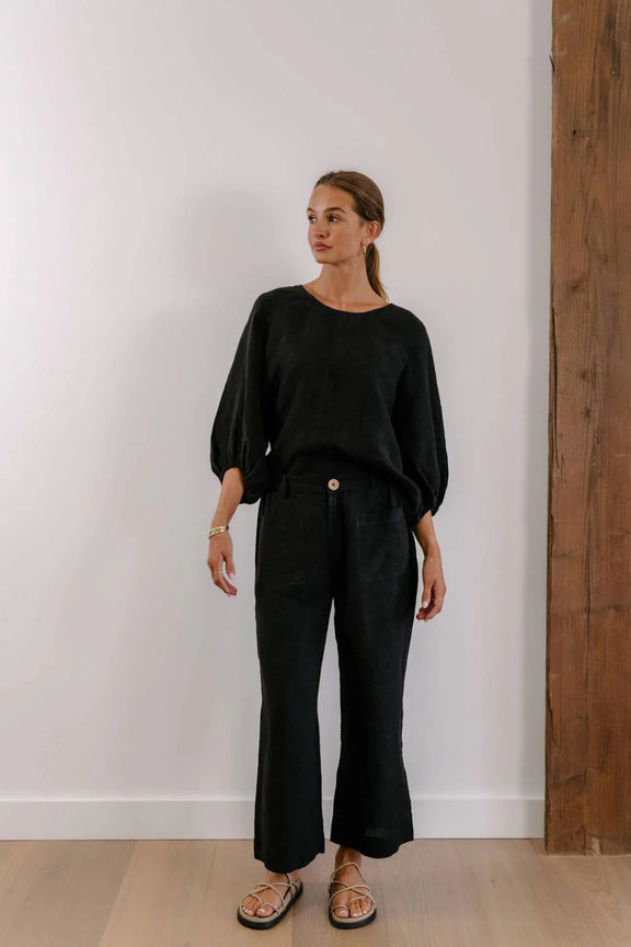 Woman wearing a black outfit standing against a white wall with wooden paneling.