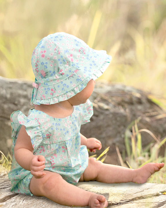 Baby in floral outfit and sun hat sitting on a log outdoors - toshi floral mint frill design