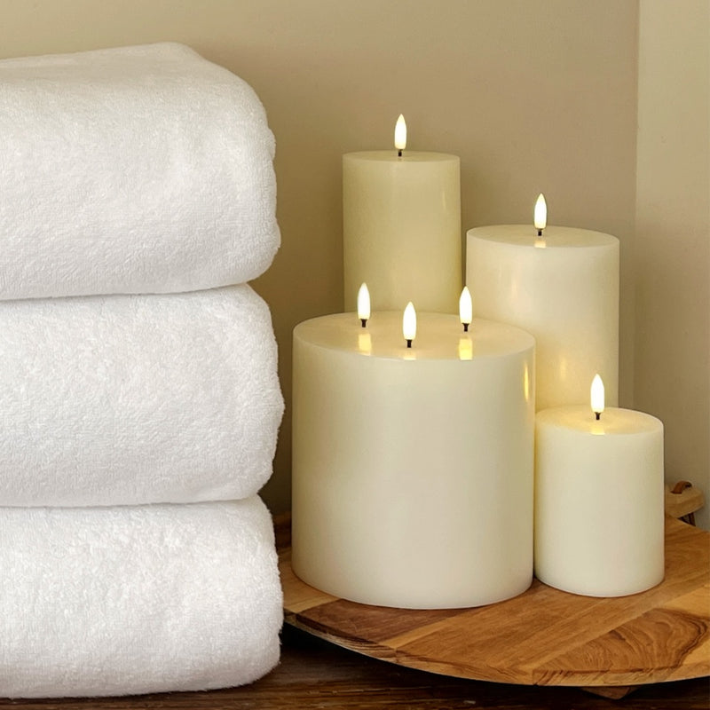 Stack of white towels next to lit flameless candles on a wooden surface.