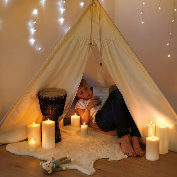 Child reading a book inside a cozy tent with flameless candles and string lights.