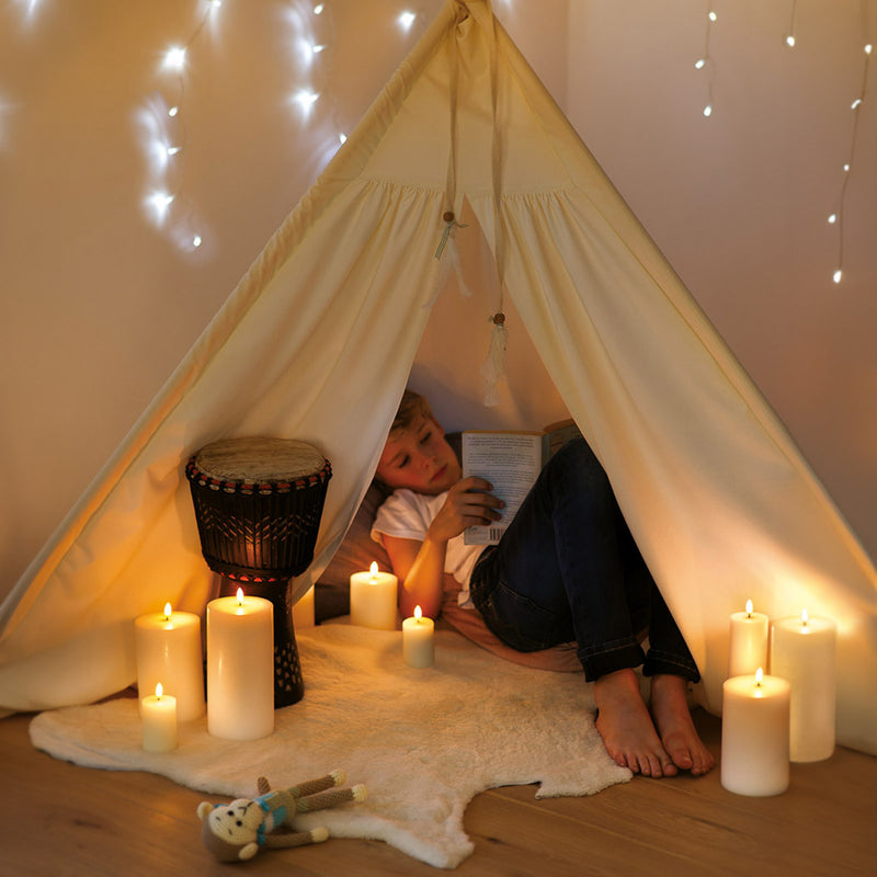 Child reading a book inside a cozy tent with flameless candles and string lights.