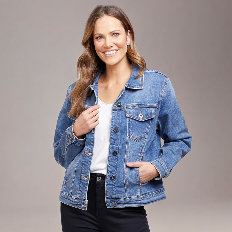 A woman smiling and wearing a blue denim jacket with a white top and black pants.
