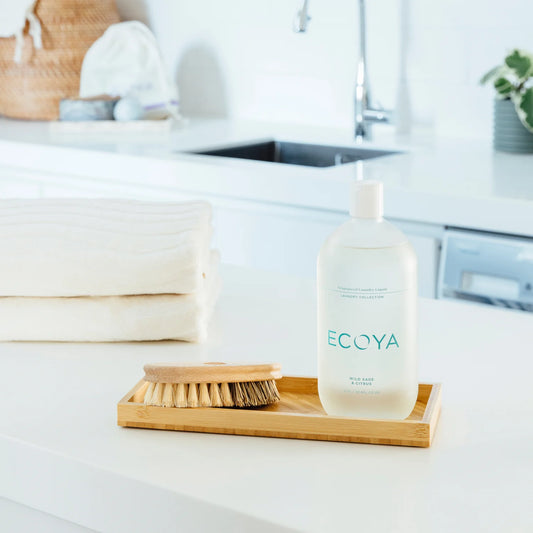ECOYA laundry liquid bottle on a bamboo tray with towels and a brush in a bathroom setting