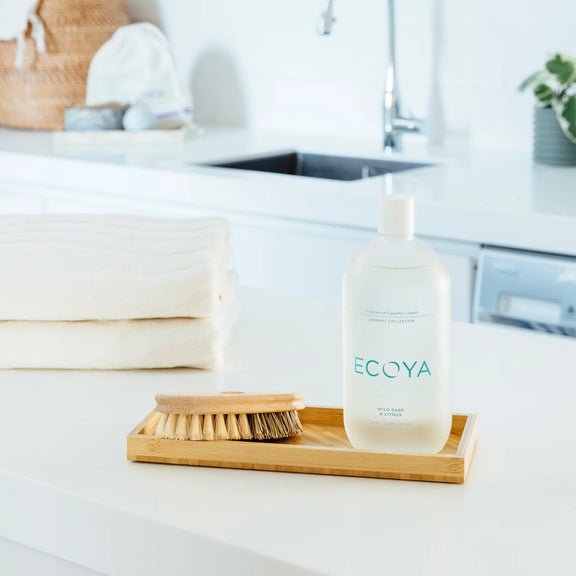 ECOYA laundry liquid bottle on a bamboo tray with towels and a brush in a bathroom setting