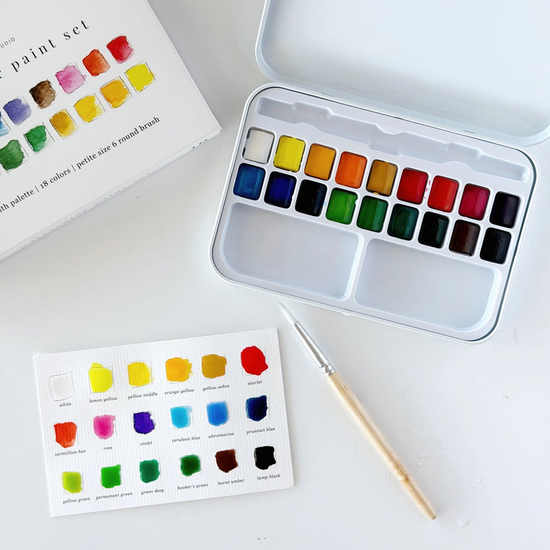 Open watercolour tin showing 18 paint colours and swatching card